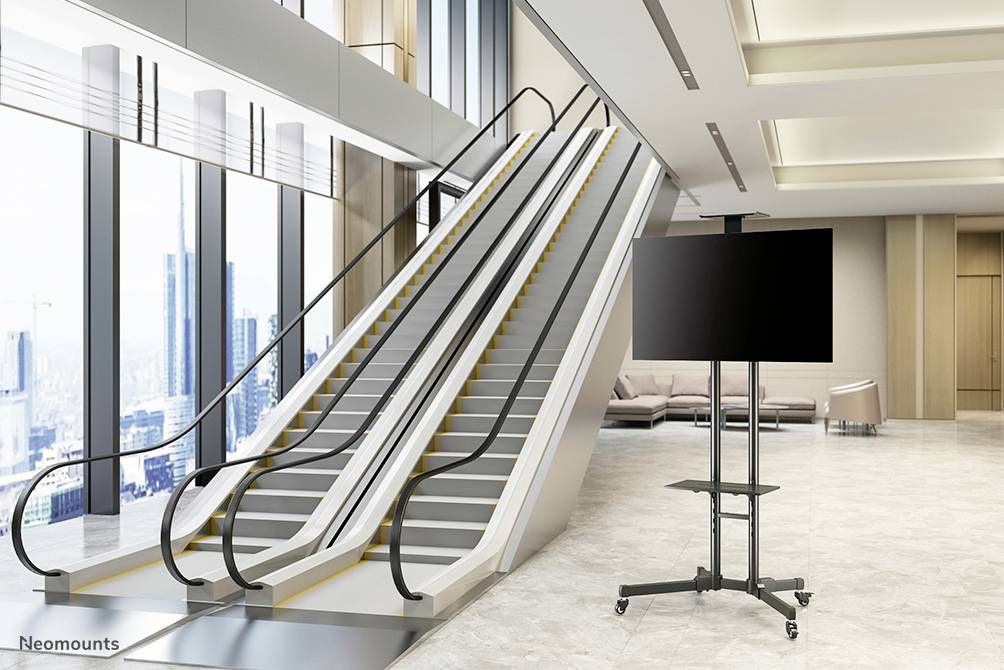 An empty escalator in a modern building with large windows and a city view in the background. On the right, an empty screen stands on a stand.