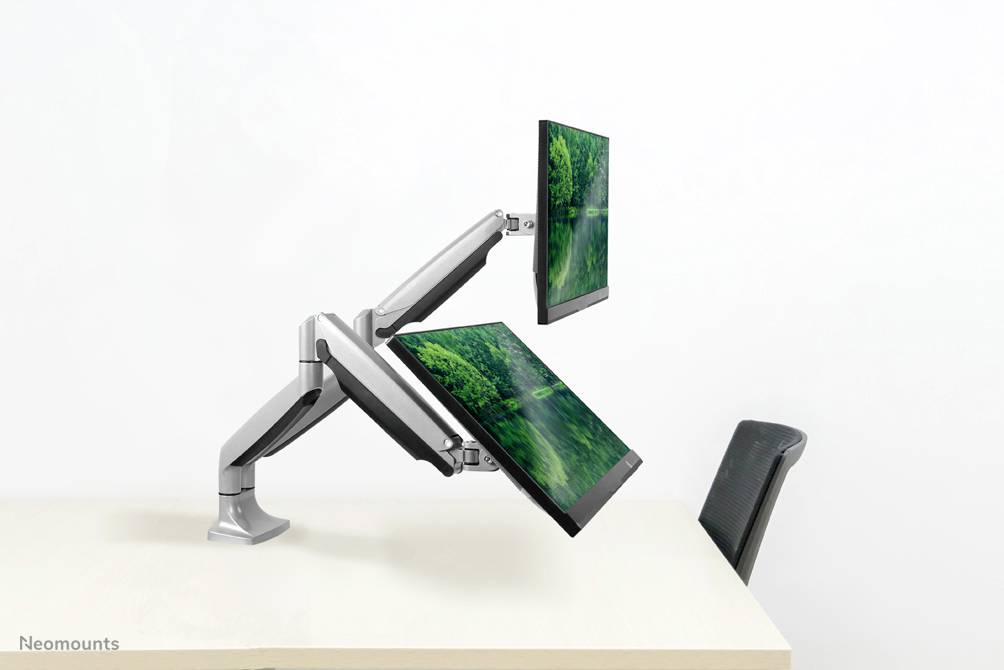 Two adjustable monitor arms hold two screens above a white desk. The background is simple and minimalist.