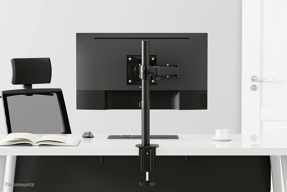A modern, ergonomic desk with a monitor arm, on which a screen is mounted. Beside it a chair and an open book.