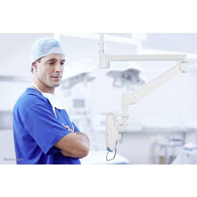 A surgeon in blue surgical attire stands with folded arms in an operating theatre, next to a mounted medical device.