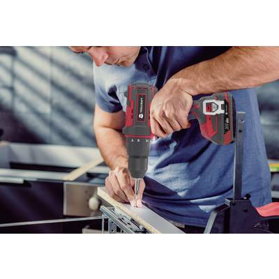 A man is using a cordless drill to turn a screw into a piece of wood in a workshop environment.