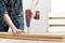 A person wearing a checked shirt is drilling a hole in a wooden board with a red cordless drill in a workshop setting.