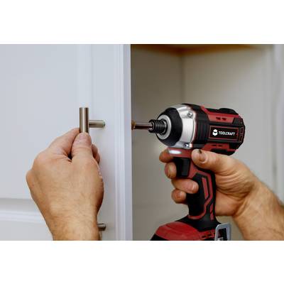 A person is installing a door handle with a red cordless drill. The handle is being fitted to a white cabinet door.