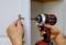A person is installing a door handle with a red cordless drill. The handle is being fitted to a white cabinet door.