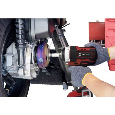 Close-up of hands wearing gloves using an impact driver to work on a motorcycle wheel.