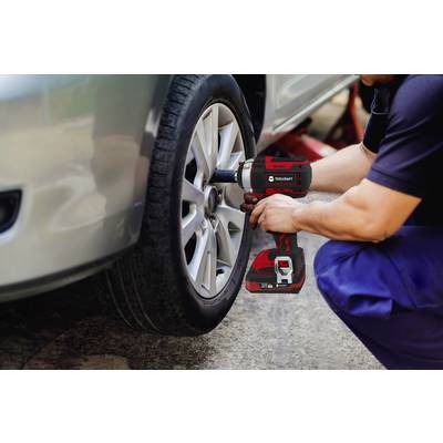 A person is changing a tyre on a car using an electric tool. The car is raised on a jack.