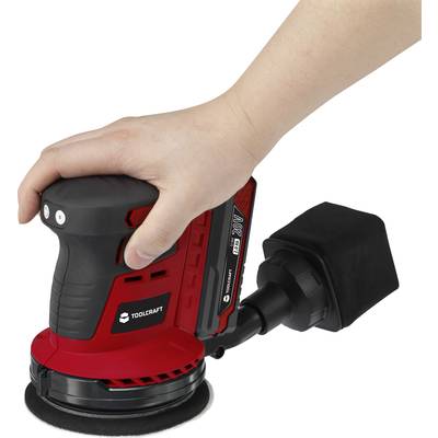 A hand is operating a red Toolcraft electric grinder, powered by a 20V lithium-ion battery.
