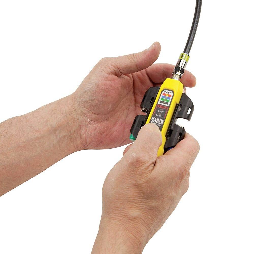 Two hands are holding a yellow electrical testing device with a cable. The device is being inspected or calibrated.