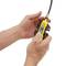 Two hands are holding a yellow electrical testing device with a cable. The device is being inspected or calibrated.