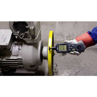 A person is measuring the vibrations of an electric motor using a vibration measuring device. The motor has a yellow protective guard.