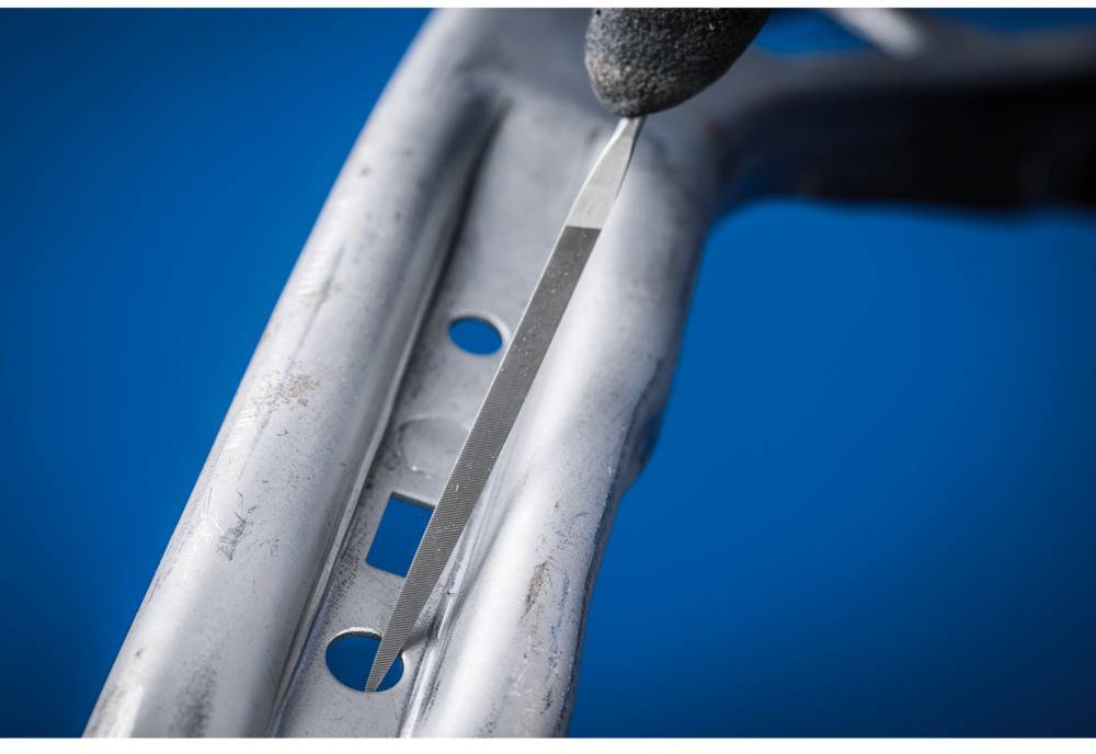 'Close-up of a metal frame with multiple openings, with a narrow strip of adhesive tape being applied to it. A gloved hand is holding the tape.'