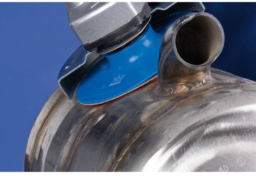 A blue grinding wheel is machining a metallic cylinder. The surface is being ground down to smooth or refine it.