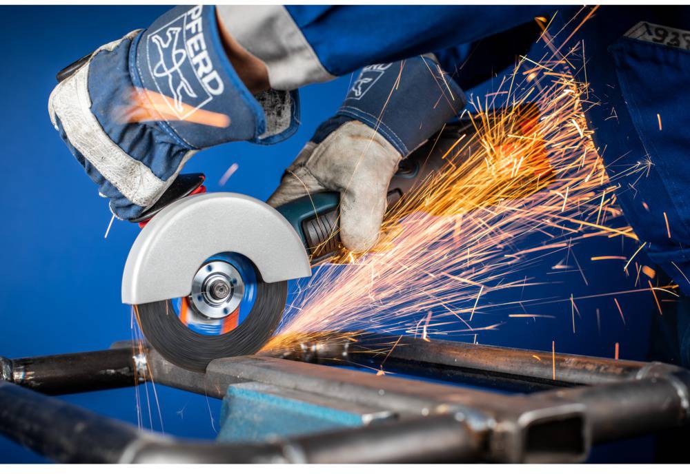 A worker in protective clothing grinds metal with an angle grinder, sparks flying. Activity of metal grinding.