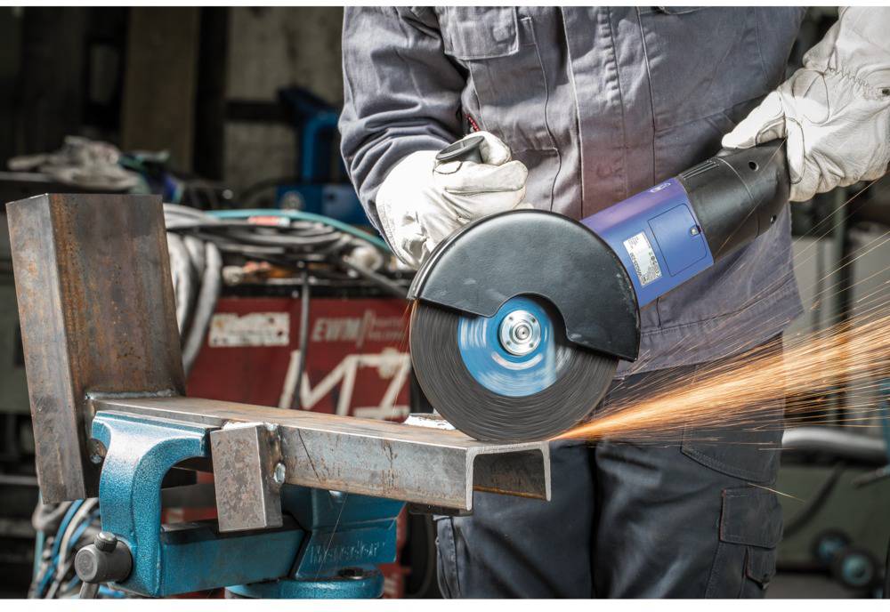 A person is cutting a piece of metal with an angle grinder on a workbench. Sparks are flying from the cutting area.