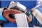 An angle grinder with a grinding disc is processing a metal edge. The person is wearing blue safety gloves against a blue background.