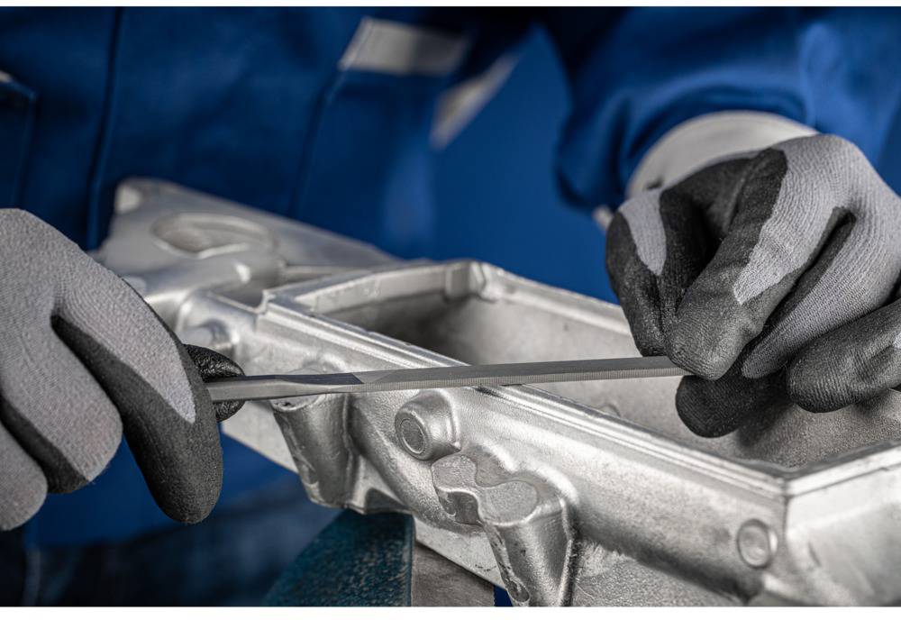 Close-up of two hands wearing work gloves manipulating a metal workpiece with a tool.