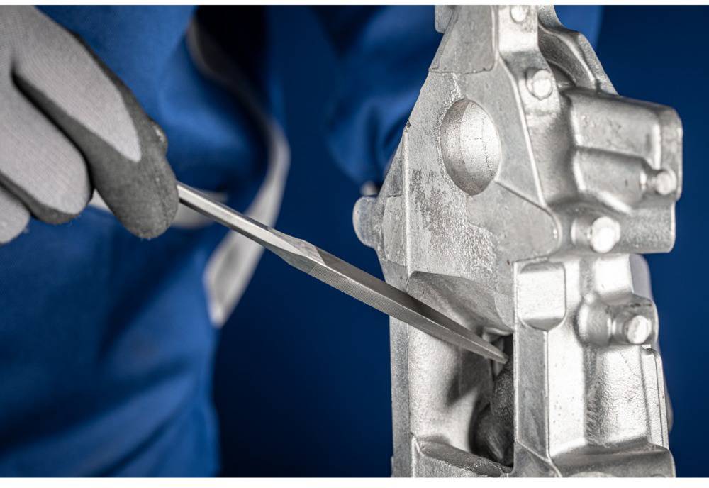 A person is filing a metal part while wearing protective gloves. The focus is on precision and safety at work.