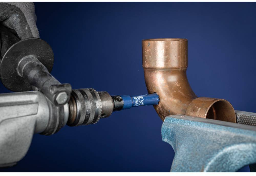 A hand holds a drill with an attachment cutting a copper pipe in a vice, symbolising craftsmanship or plumbing installation.