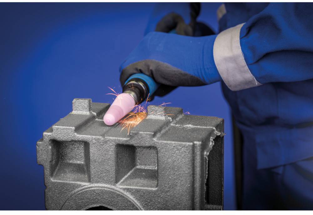 A person is grinding metal with an angle grinder. Sparks are flying from the sand-coloured grinding point. Gloves and protective clothing.
