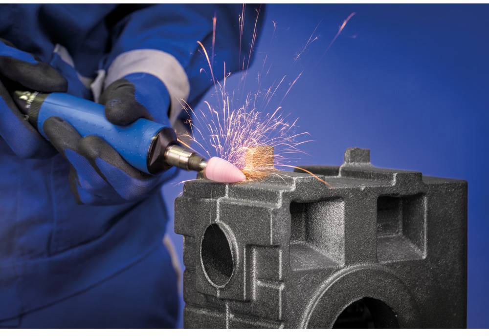 A person is grinding metal with an angle grinder, causing sparks to fly. The person is wearing blue protective clothing and gloves.