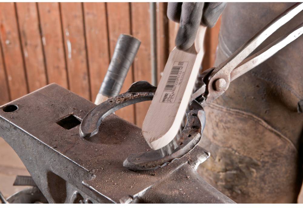 A person is using a wire brush spanner to keep a horseshoe clean on an anvil. Rustic workshop environment.