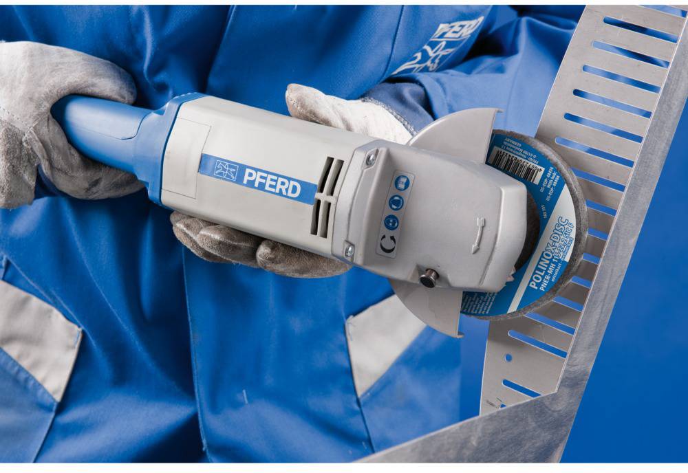 A person wearing protective equipment is holding an angle grinder with a blue grinding disc, ready for metalworking.