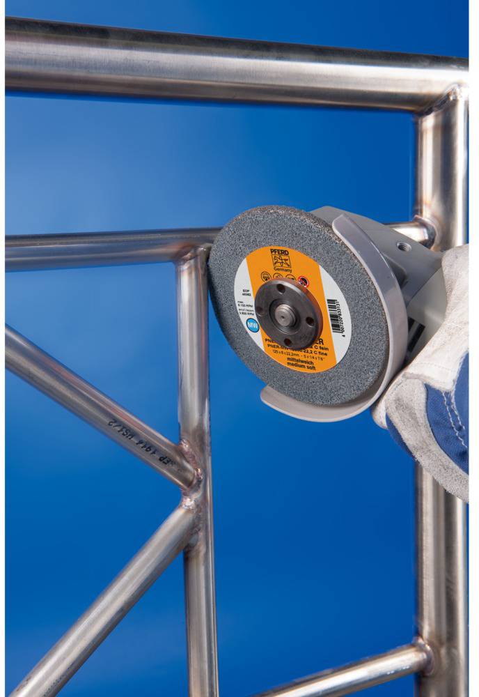 A person is using an angle grinder to smooth a metal edge. The person is wearing protective gloves.