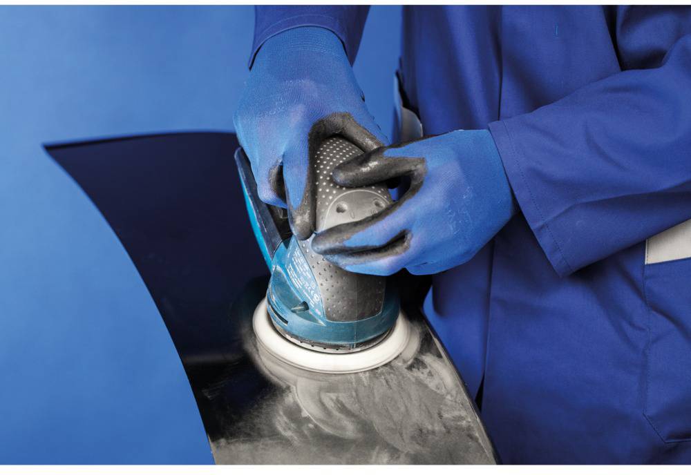A person is grinding a black metal surface with an electric grinding machine, wearing blue gloves and work clothing.