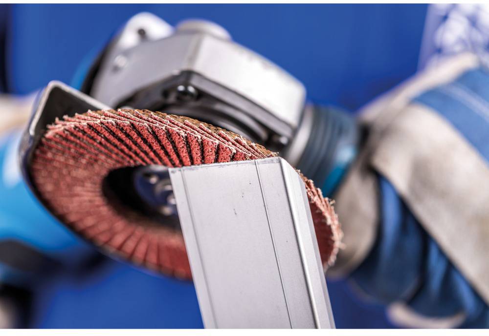 Close-up of an angle grinder with a grinding disc, being operated by a person wearing blue gloves and working on a piece of metal.
