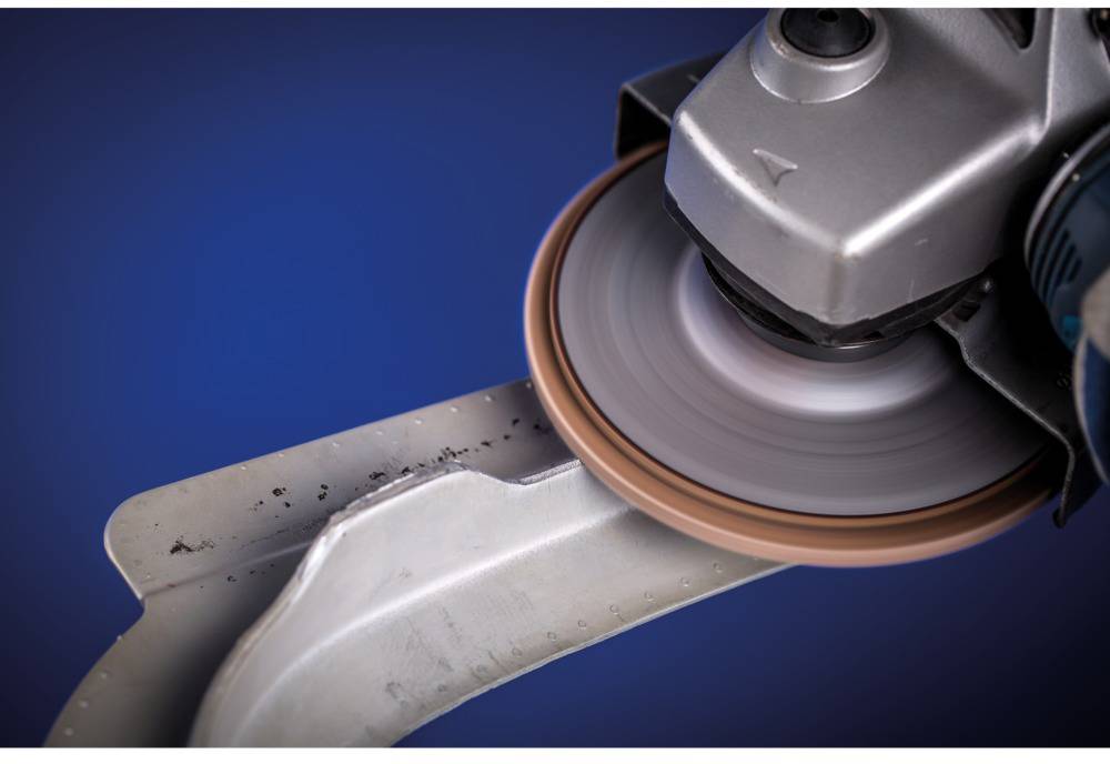 Metal grinding machine smoothing a curved metal edge, with a rotating grinding wheel against a blue background.