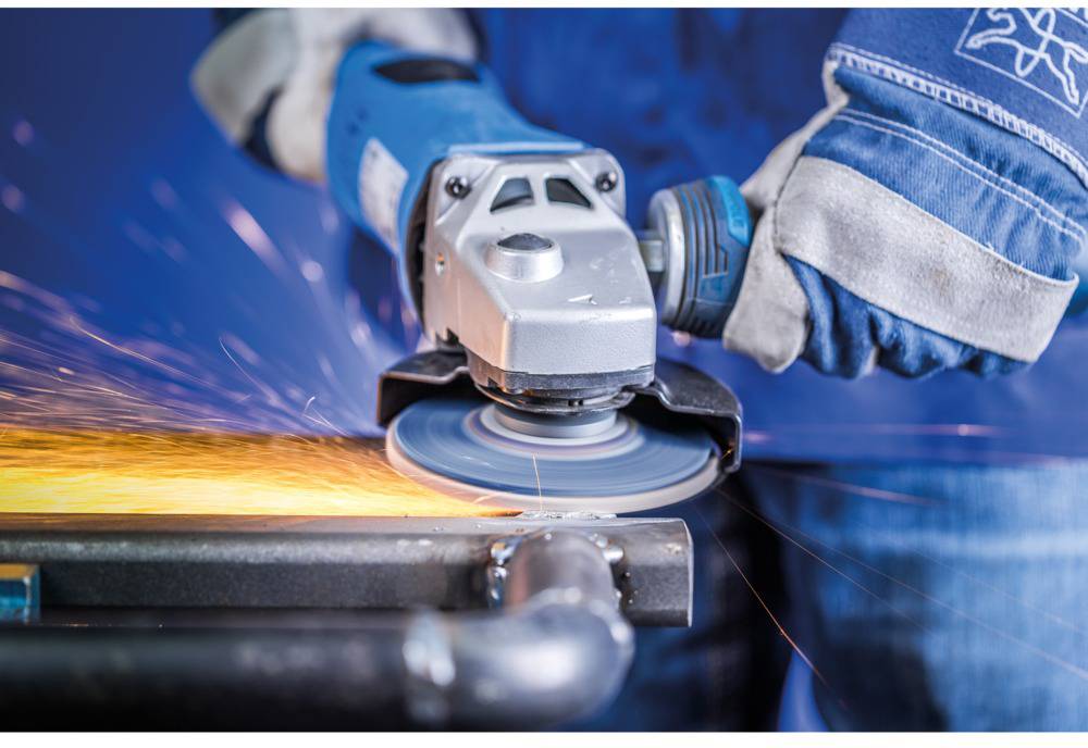 A person is wearing blue protective gloves and grinding metal with an angle grinder, with sparks flying.