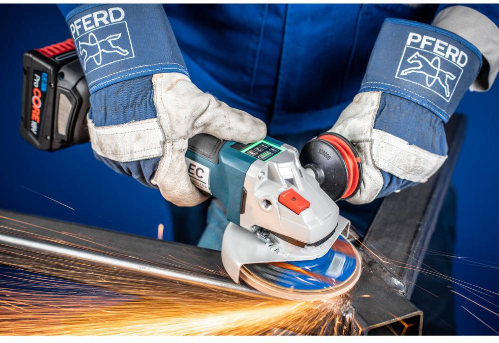 A person wearing protective clothing grinds metal using an angle grinder. Sparks are flying during the grinding process.