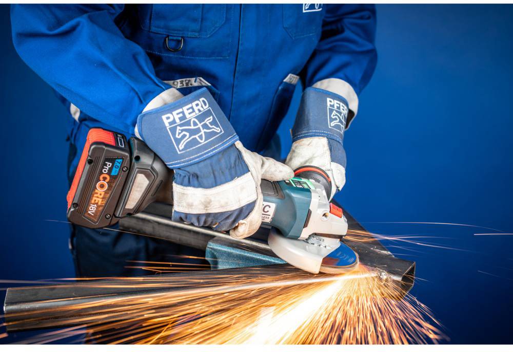 A person in blue workwear is grinding metal with an angle grinder, sparks flying.