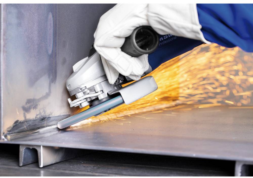 A person is grinding a metal edge with an angle grinder. Sparks are flying, indicating intensive processing.
