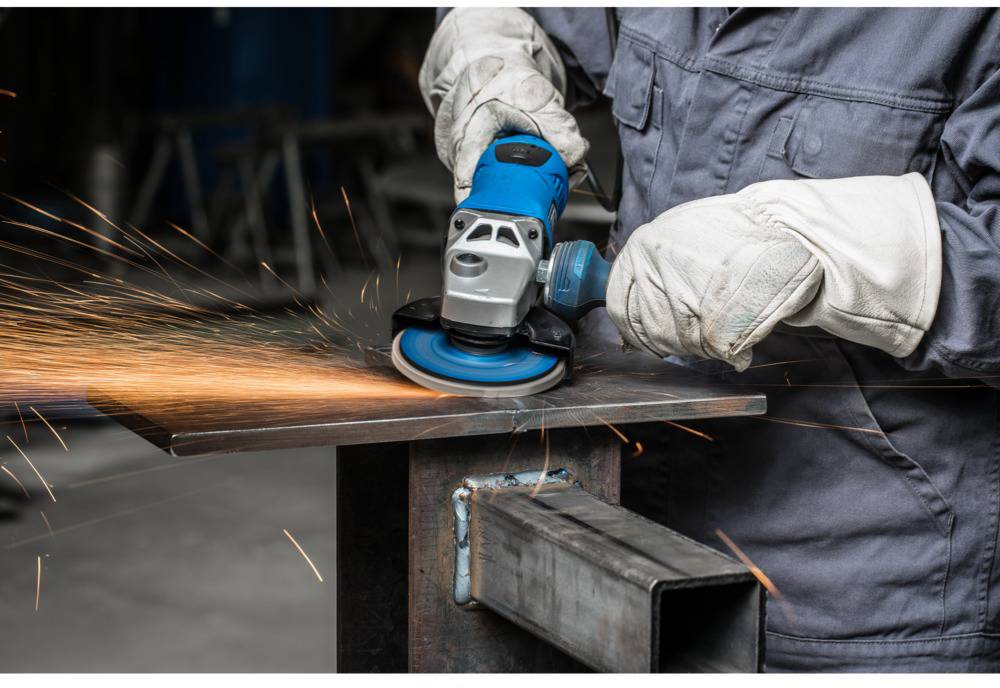 A person in protective clothing is grinding metal with an angle grinder. Sparks are flying off the metal piece.