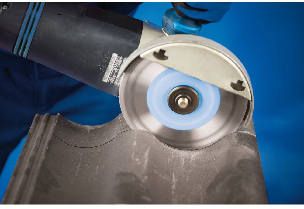 A person is cutting a grey roof tile with an angle grinder. Sparks are flying, demonstrating the active processing of the material.