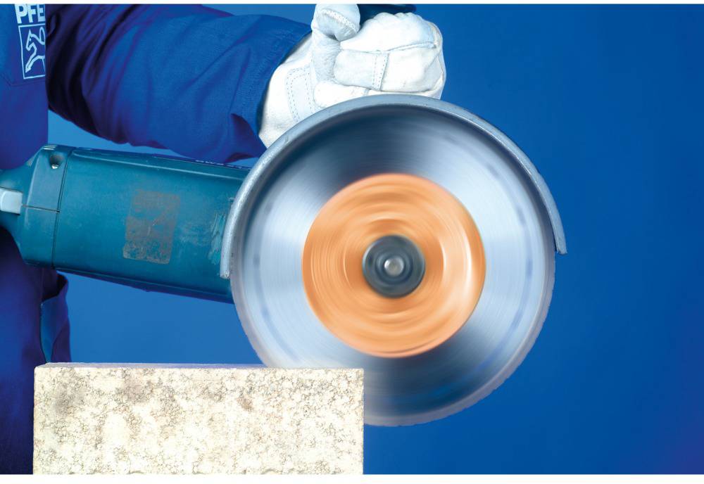A person wearing blue work gloves is using a powerful circular saw to cut a roughly textured stone slab.