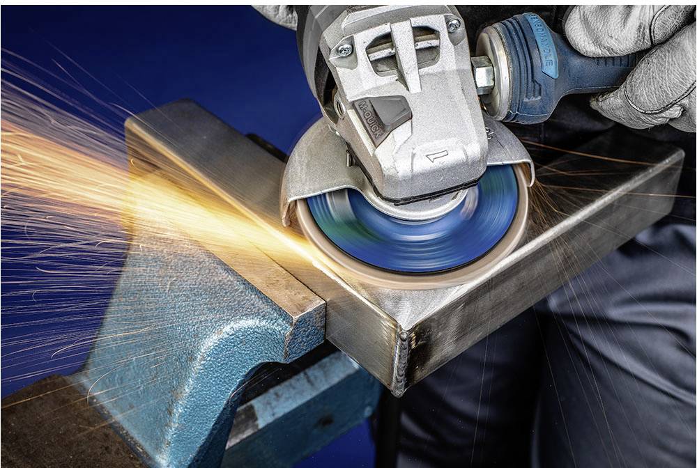 A person is grinding metal with an angle grinder. Sparks are flying from the grinding point.