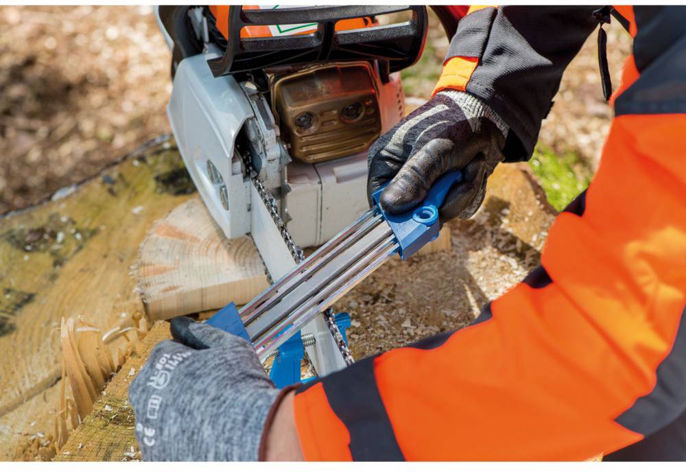 A person wearing protective gloves and clothing sharpening a chainsaw on a wooden log.