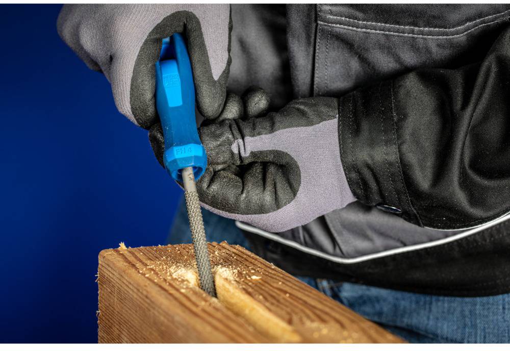 A person is working with a file on a piece of wood. They are wearing gloves and using a blue file. Wood shavings are visible.