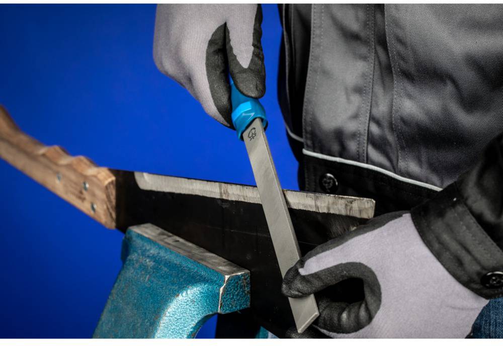 A person wearing gloves is sharpening a saw with a file. The saw is clamped in a blue vice.