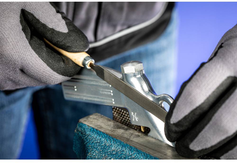 Close-up of hands in gloves grinding an ice blade with a small tool. Background is blurred and blue.