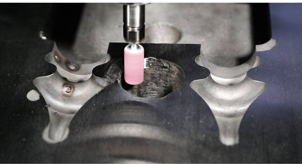 'Close-up of a milling machine precisely machining metal. The milling head is pink and is working on a dark metal workpiece.'
