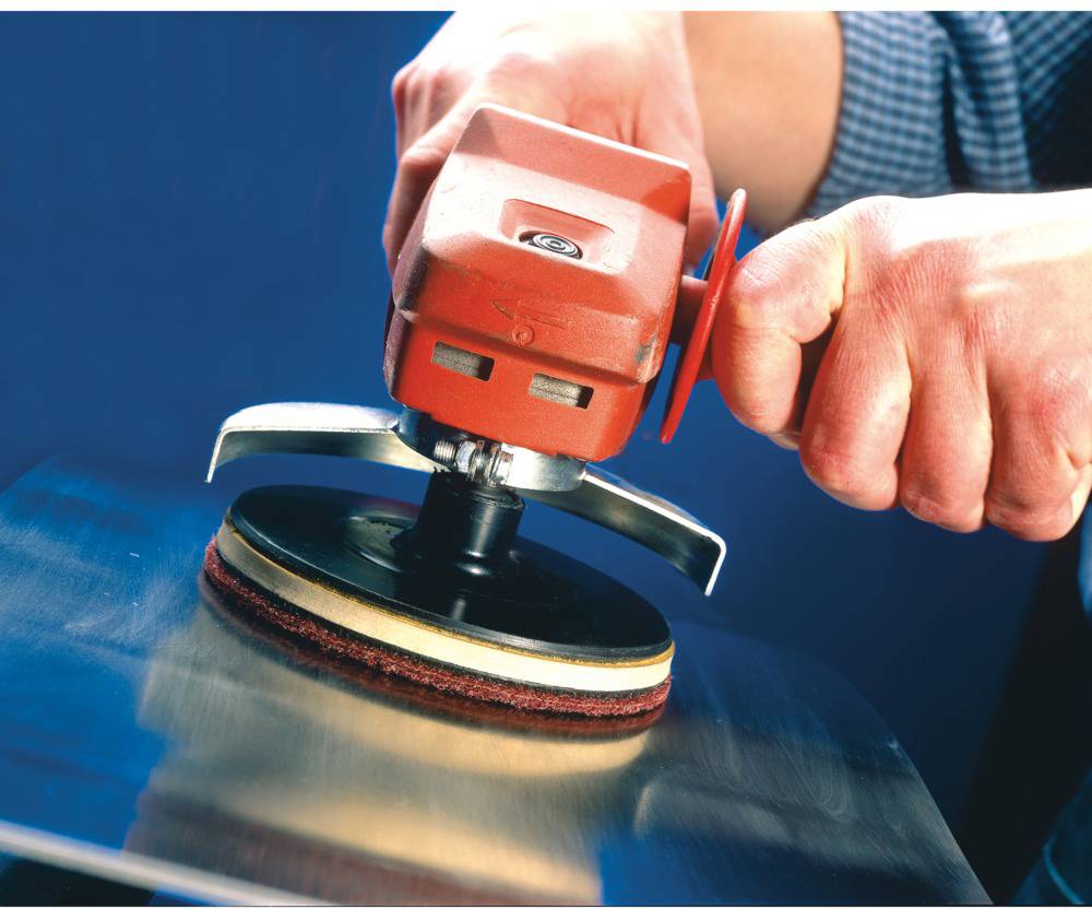A person is polishing a metal surface with a rotating polishing machine. Their hands are holding the device firmly while it operates.
