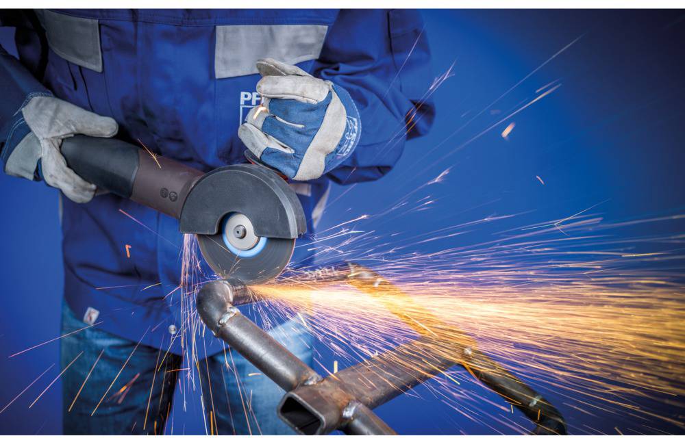 A person in protective clothing is using an angle grinder to cut metal. Sparks are flying in all directions.