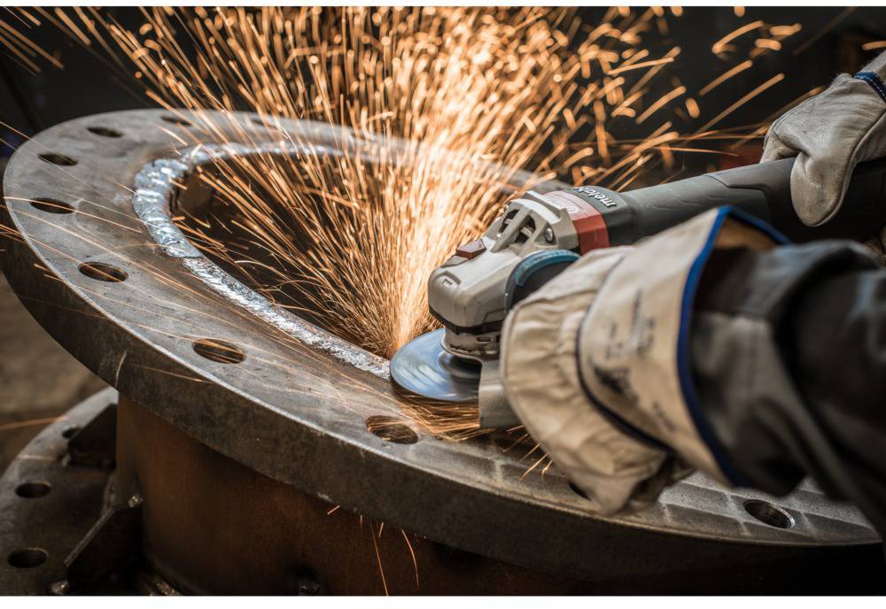 A person is grinding metal with an angle grinder, sparks flying. Protective gloves are being worn.
