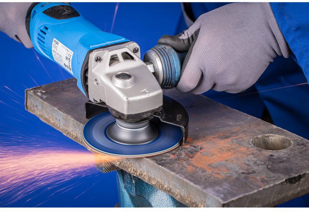 Two hands wearing grey gloves are holding an angle grinder, generating sparks as it grinds across a piece of metal.