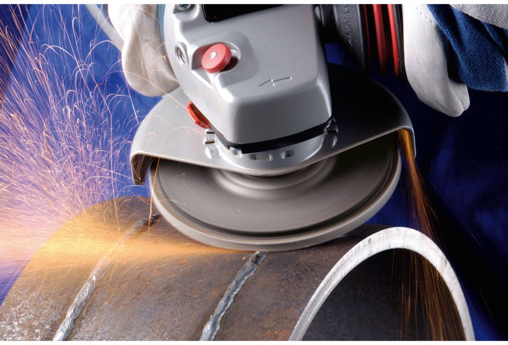 A person is grinding a metal tube with an angle grinder, with sparks flying. Protective clothing is being worn.