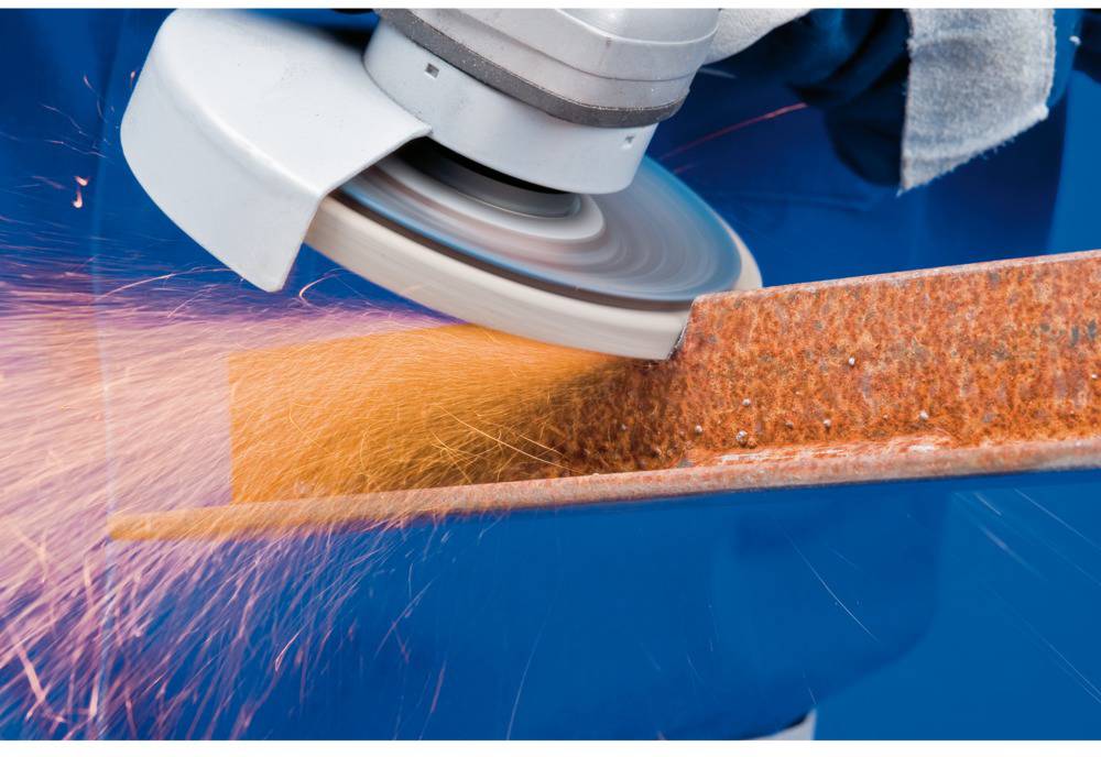 A grinding machine is working on a rusty piece of metal, with sparks flying. The primary action is grinding the metal.