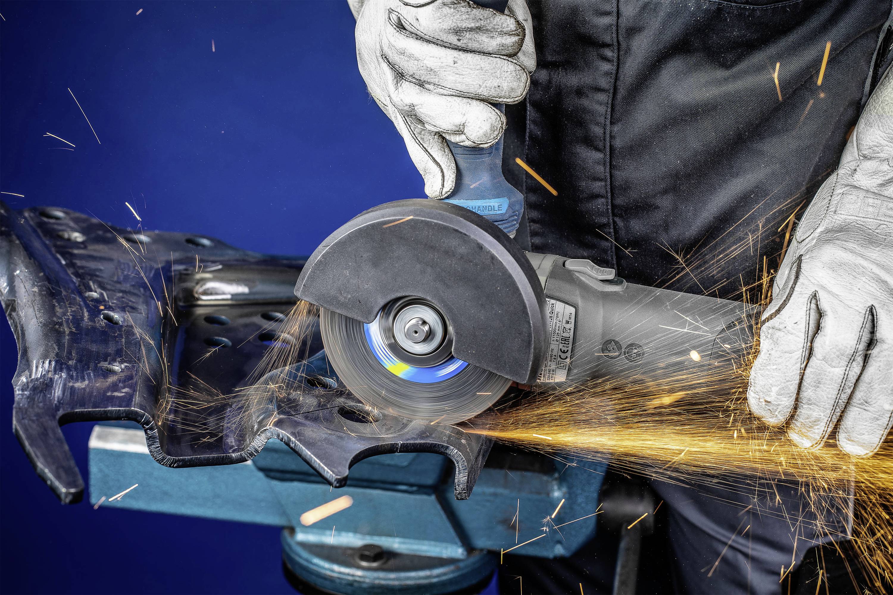 A person is grinding metal with an angle grinder, with sparks flying. The scene demonstrates workplace safety through the use of gloves.